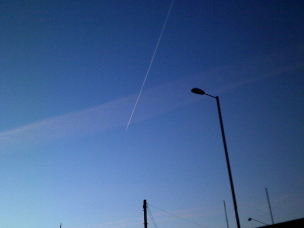 a photo looking up to the sky showing lamp posts and an airplane going by