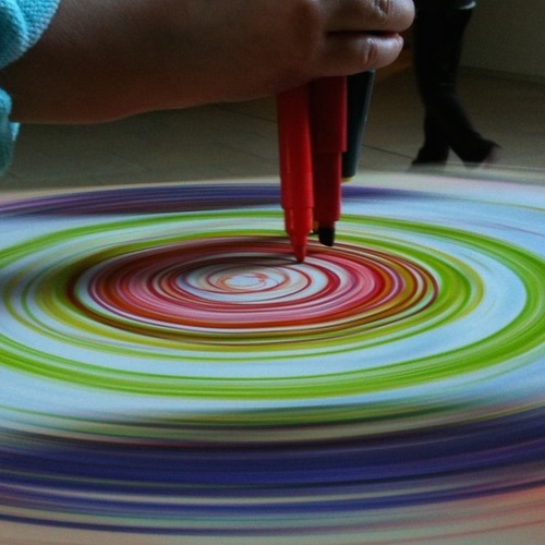 image of pens being held down while a wheel spins paper and circular marks are made on the paper