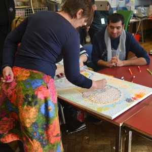 a photo of a woman working on a painting with a man looking on