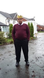 man stood in a suburban street wearing a gold crown 
