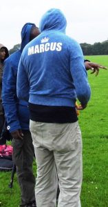 the image of two men talking with their backs to the camera, the one nearest has Marcus on the back on his blue hoodie