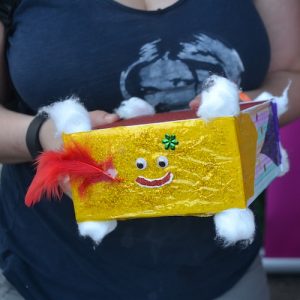 A person holding a box decorated in gold and glitter. it has a smiley face on it